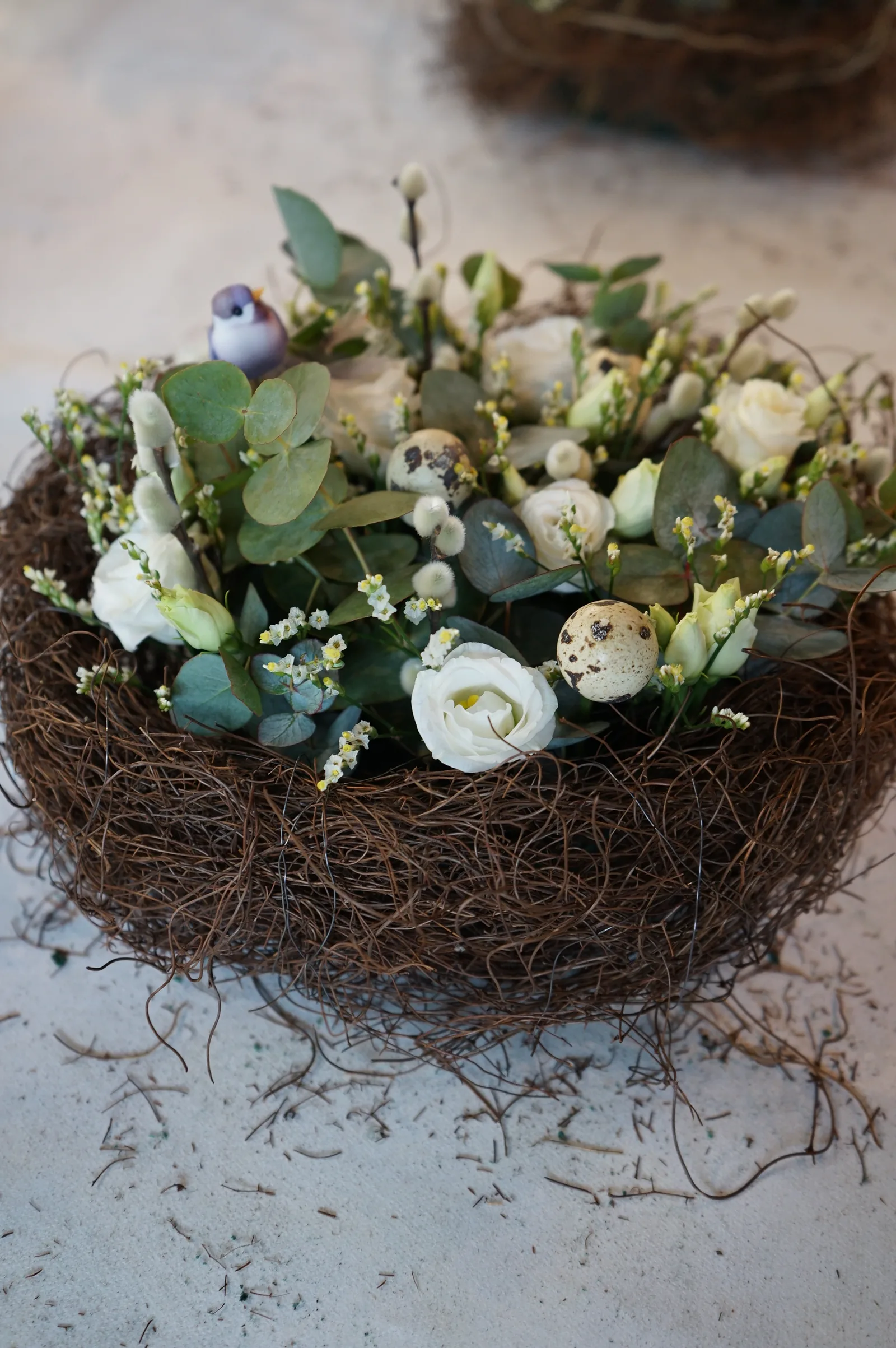 Nido di rami con lisianthus bianchi, eucalipto, uova di quaglia e un uccellino decorativo azzurro