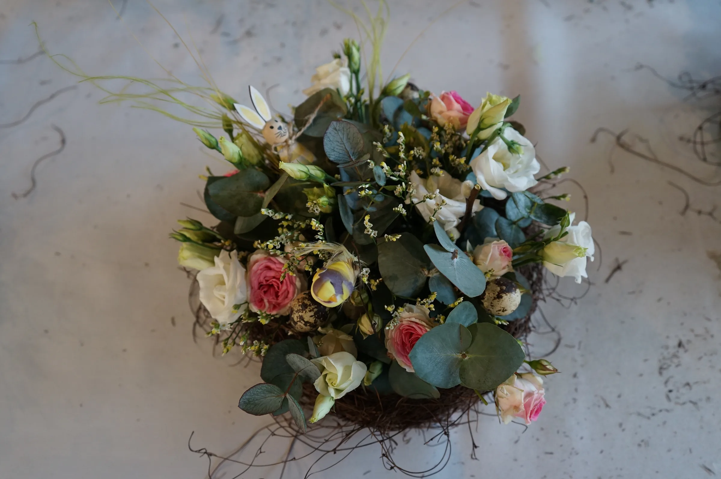Centrotavola visto dall'alto con rose rosa, lisianthus bianchi, eucalipto e un uovo decorato