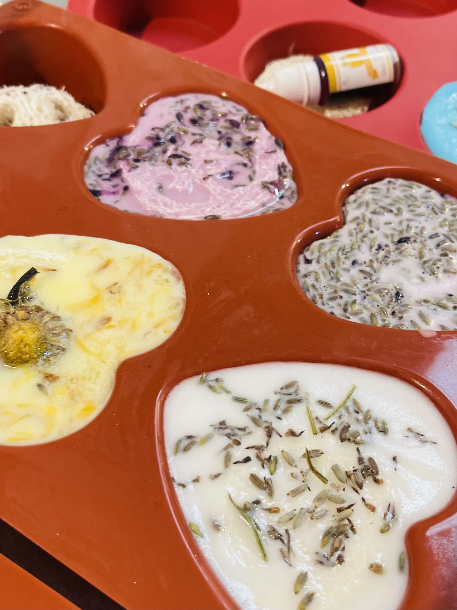 Stampi a cuore appena riempiti, con lavanda secca e un fiore giallo sopra il sapone ancora liquido