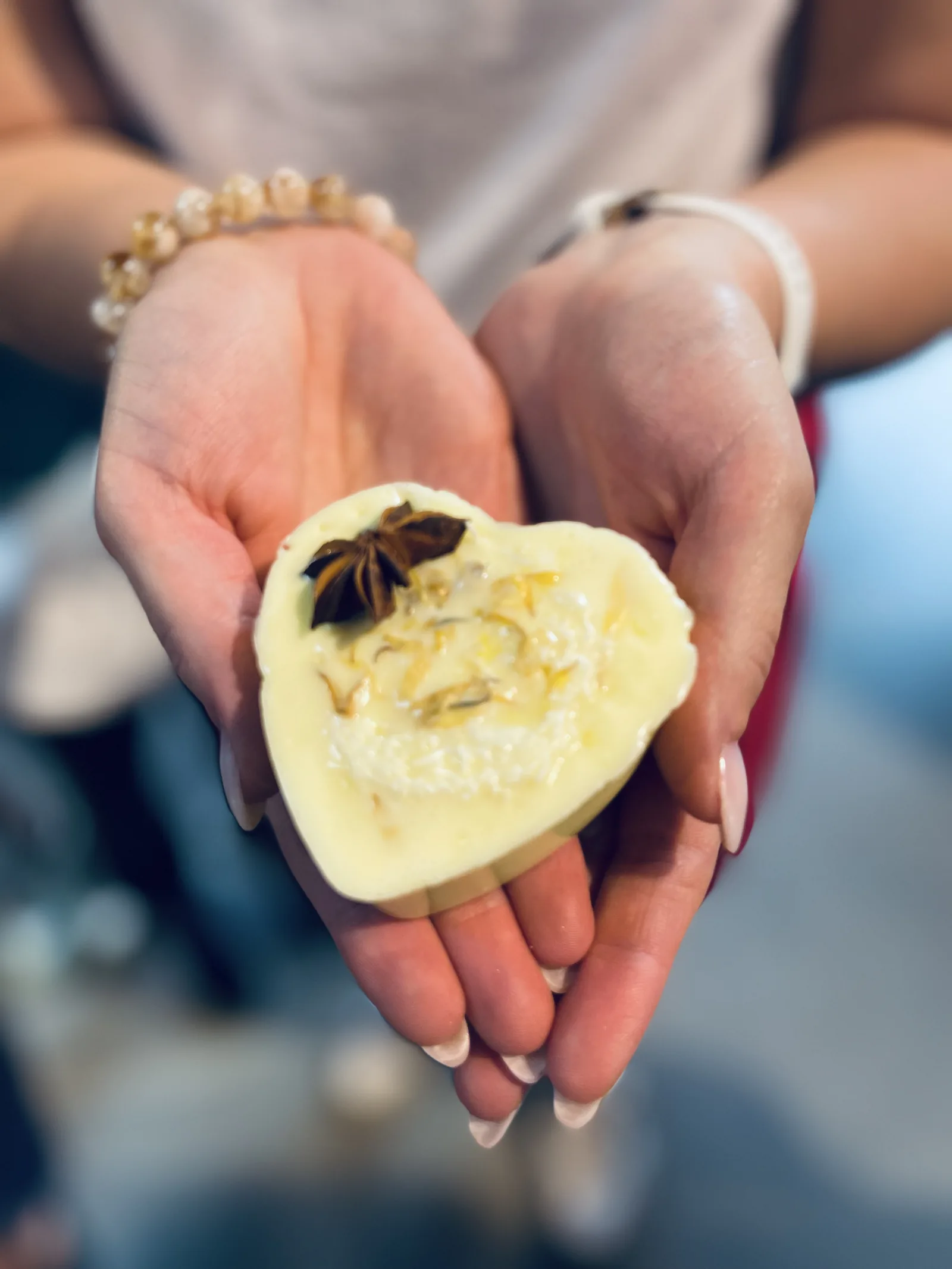 Sapone bianco a cuore con un anice stellato e petali gialli, fra due mani
