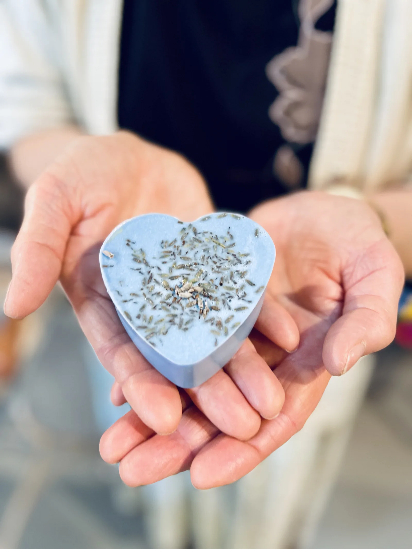 Un sapone azzurro a cuore con la lavanda sopra, tenuto fra le mani