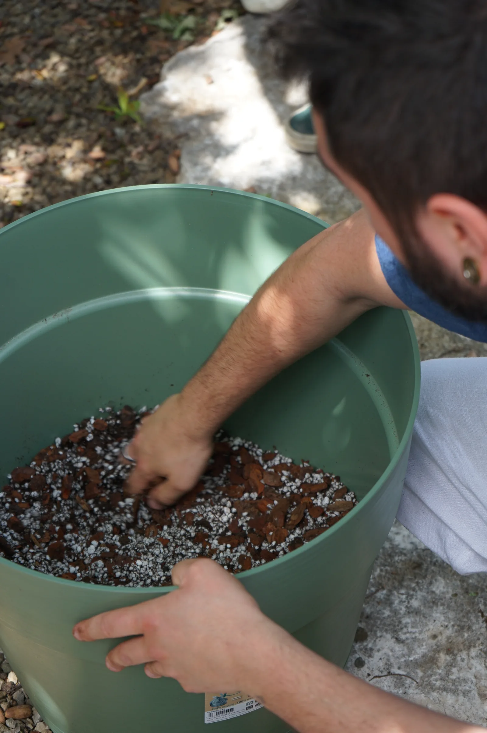 Un ragazzo mescola con la mano perlite e scaglie di corteccia dentro un grande vaso verde