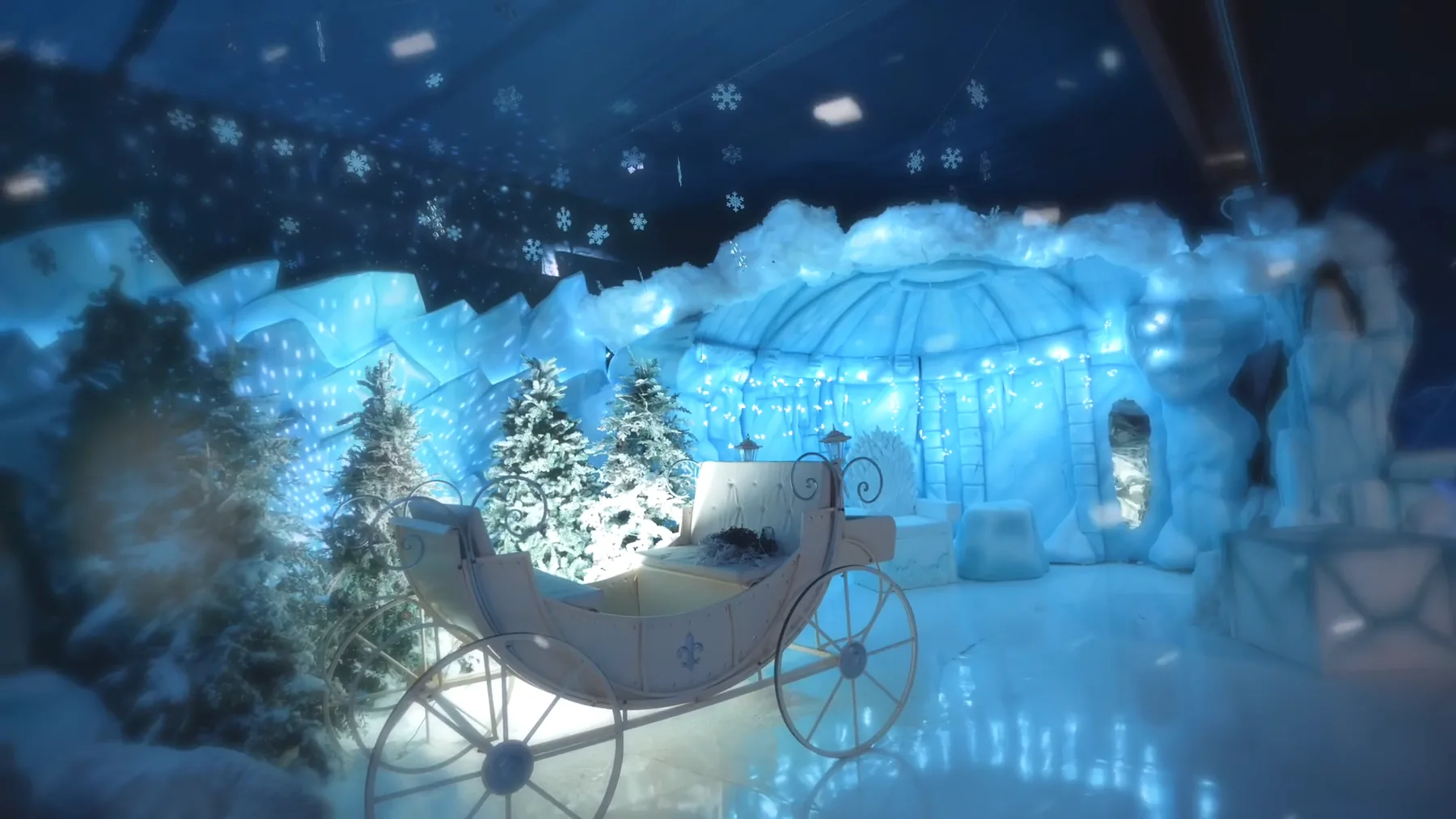 Una carrozza bianca illuminata fra abeti innevati, davanti a una scenografia di ghiaccio azzurro con un igloo, sotto un soffitto di fiocchi di neve