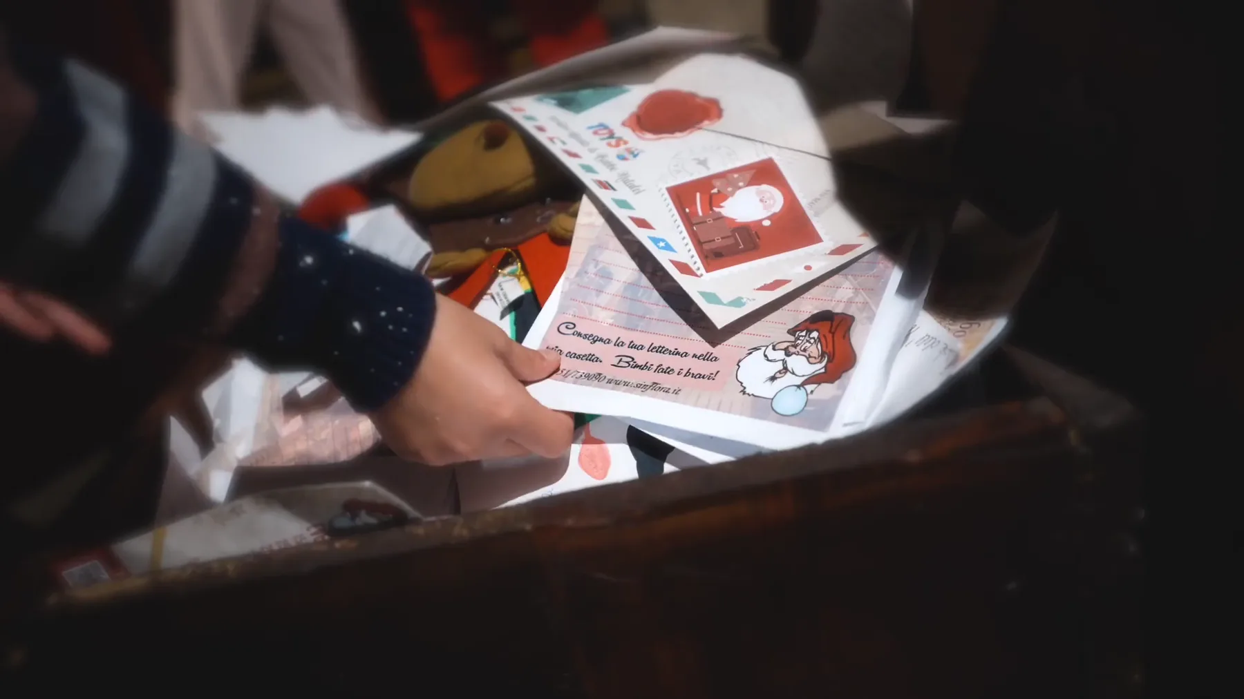 Una mano infila le letterine per Babbo Natale in una cassetta di legno illuminata