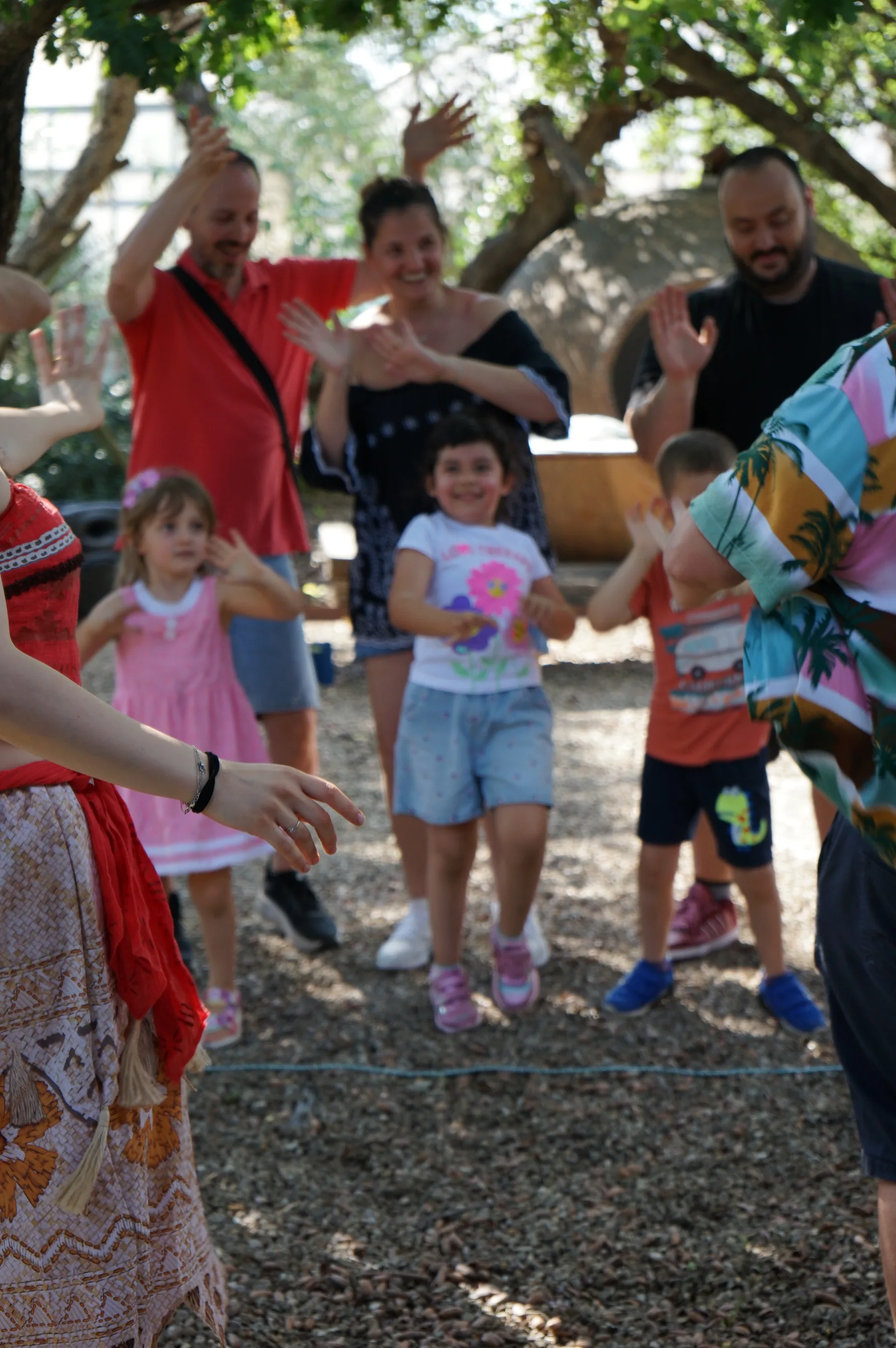 Bambini che ballano sulla ghiaia alzando le braccia, con gli adulti dietro che fanno lo stesso e il vestito di Vaiana in primo piano