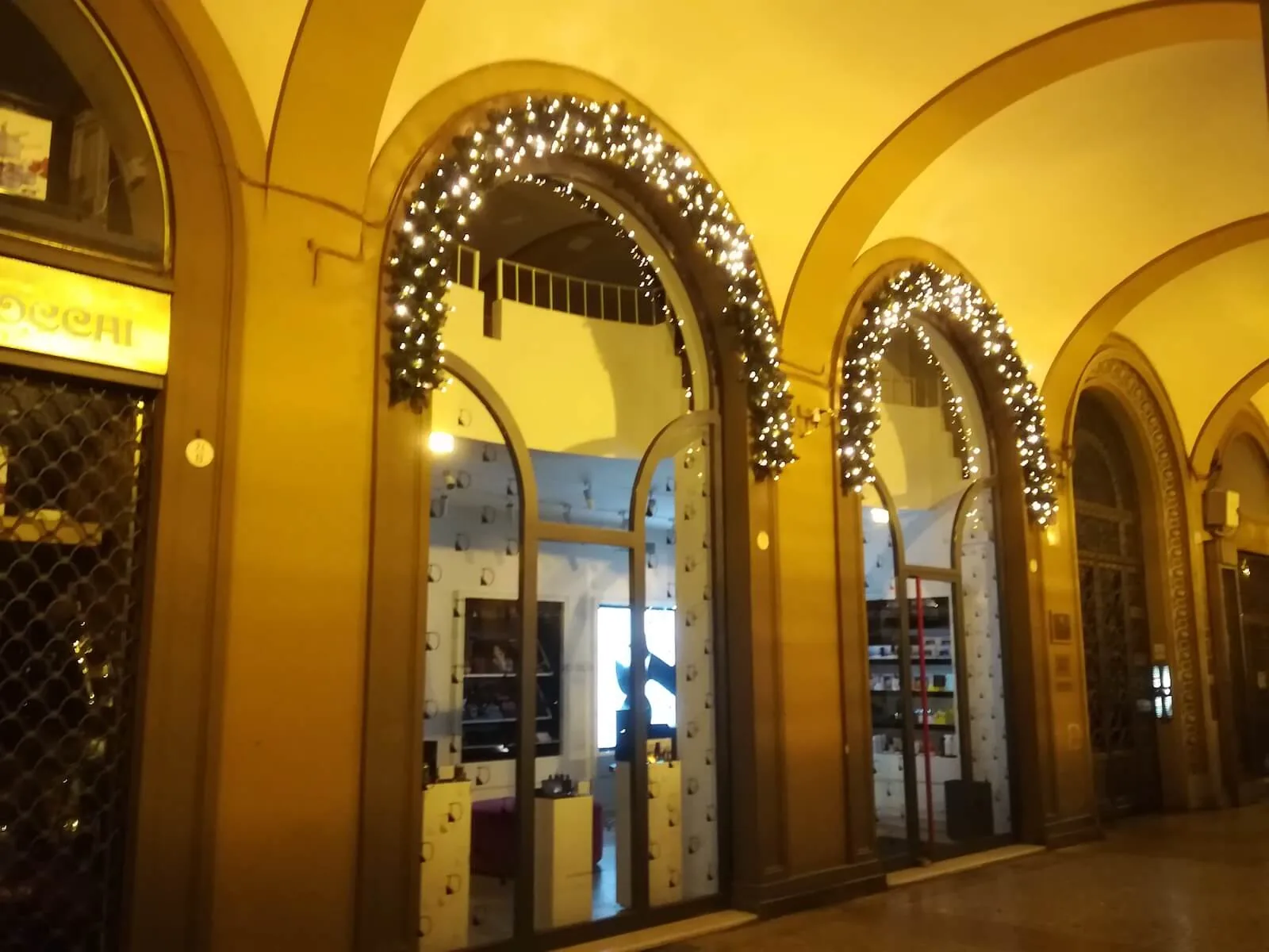 Vetrine ad arco sotto un portico, incorniciate da festoni verdi con le lucine accese