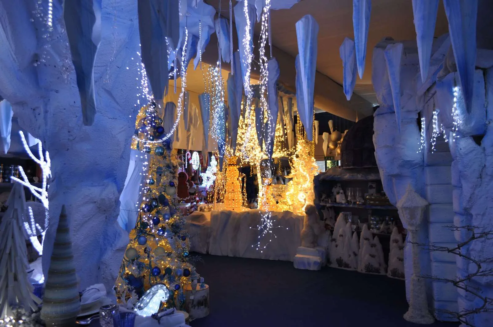 Grotta di ghiaccio con stalattiti bianche e azzurre, un albero addobbato di blu e figure di luci dorate sul fondo