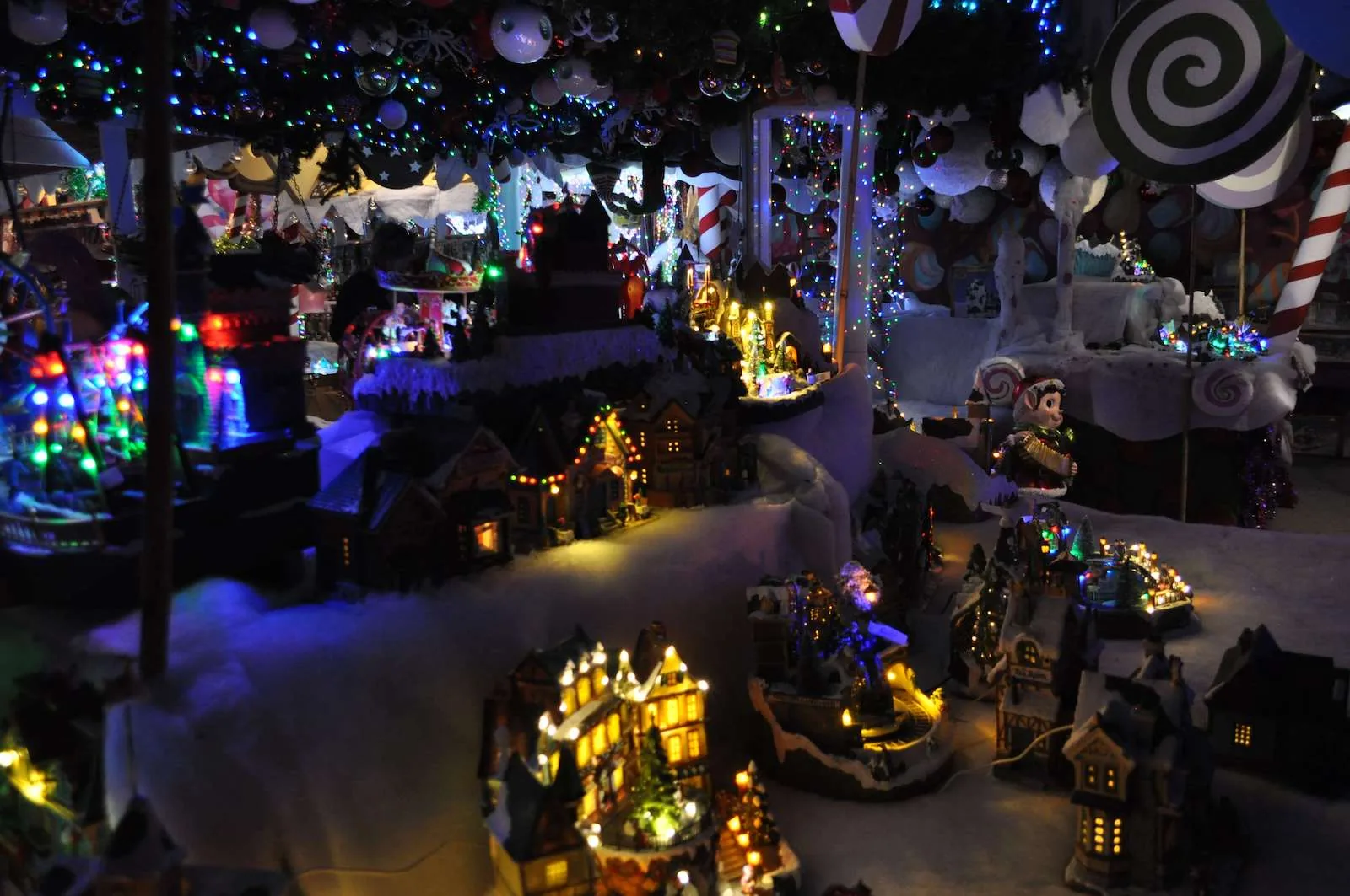 Villaggio in miniatura di casette illuminate su un paesaggio innevato, fra lecca lecca giganti