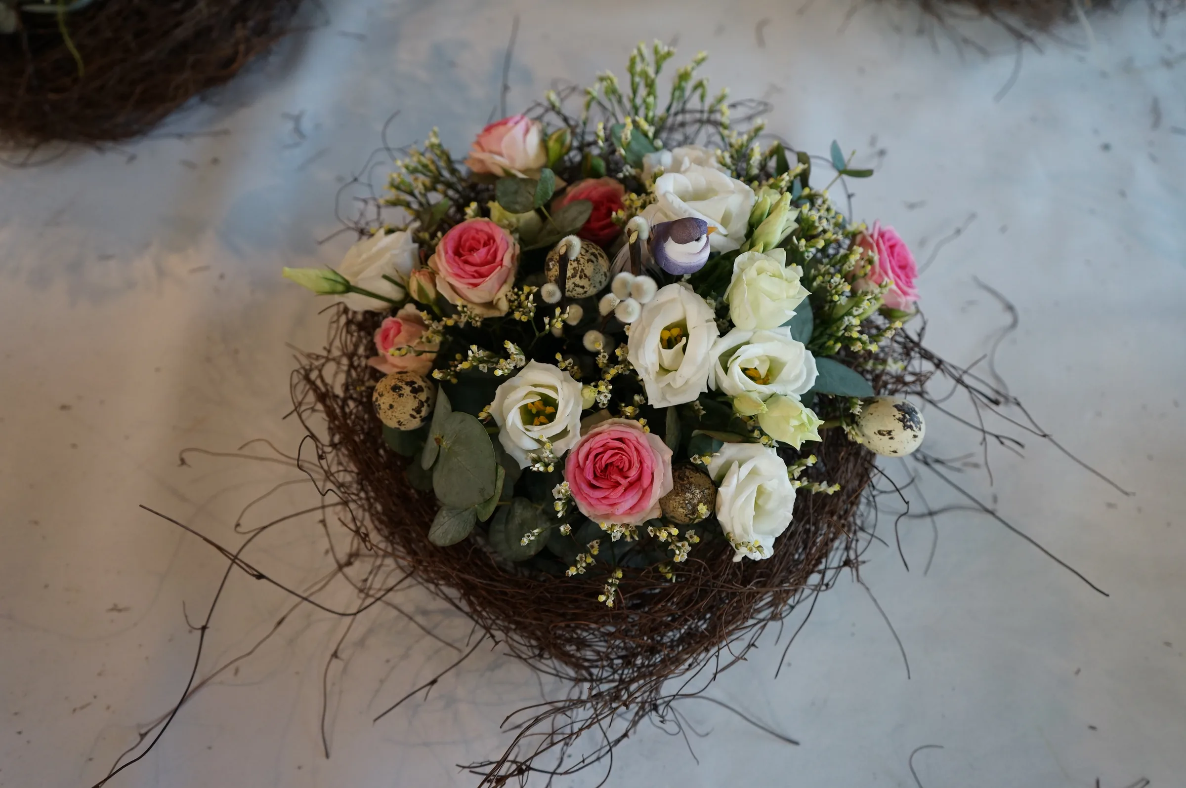 Composizione di rose, lisianthus ed eucalipto dentro un nido di rami, appoggiata su un tavolo coperto di carta bianca