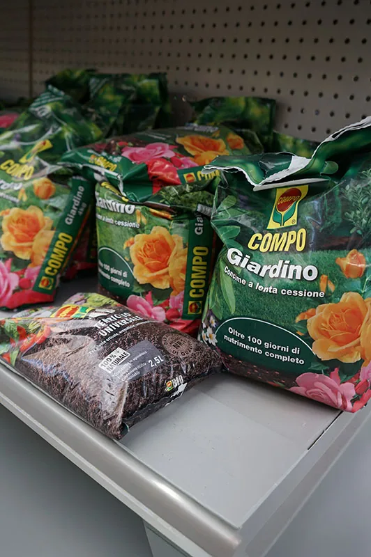 Sacchi di concime a lenta cessione per il giardino e una confezione di terriccio universale da 2,5 litri appoggiati sullo scaffale