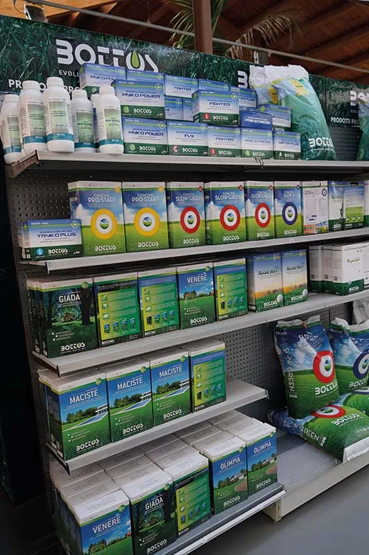 Scaffale di prodotti per il prato in scatole e sacchi verdi e bianchi, su tutti i ripiani