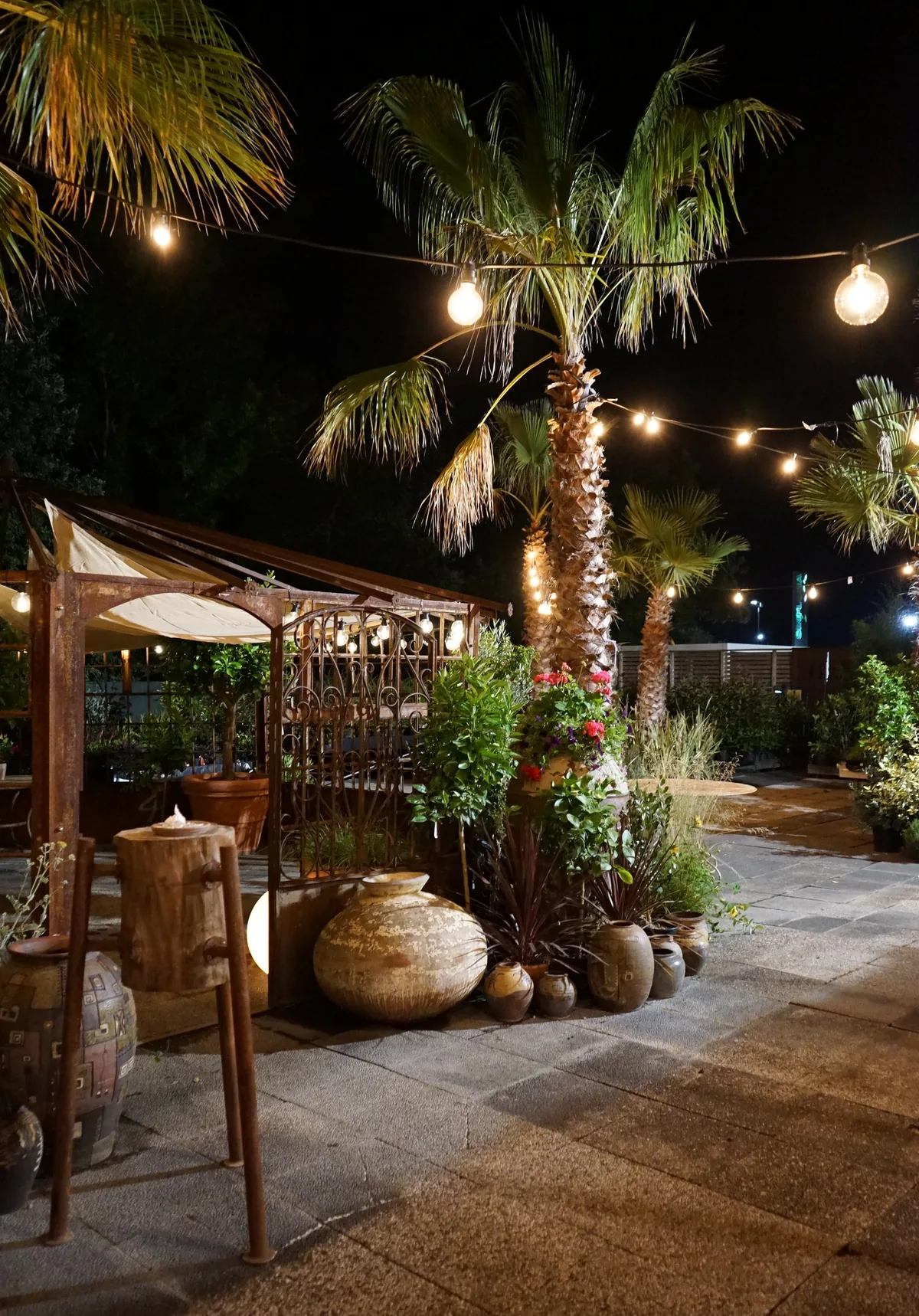 Il pergolato all'aperto di sera, con le lampadine accese fra le palme e le anfore di terracotta