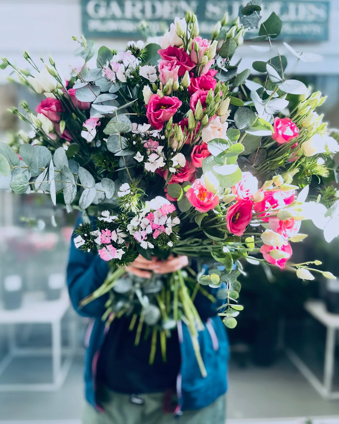 Un grande mazzo di lisianthus rosa, fucsia e bianchi con garofanini bianchi e rosa e rami di eucalipto, tenuto in braccio davanti al negozio