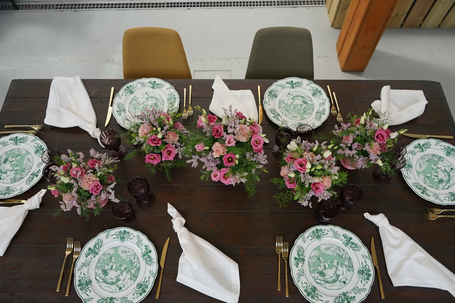 Il tavolo visto dall'alto: piatti a decoro verde, tovaglioli bianchi e composizioni di lisianthus rosa, garofani color pesca e limonium lungo il centro