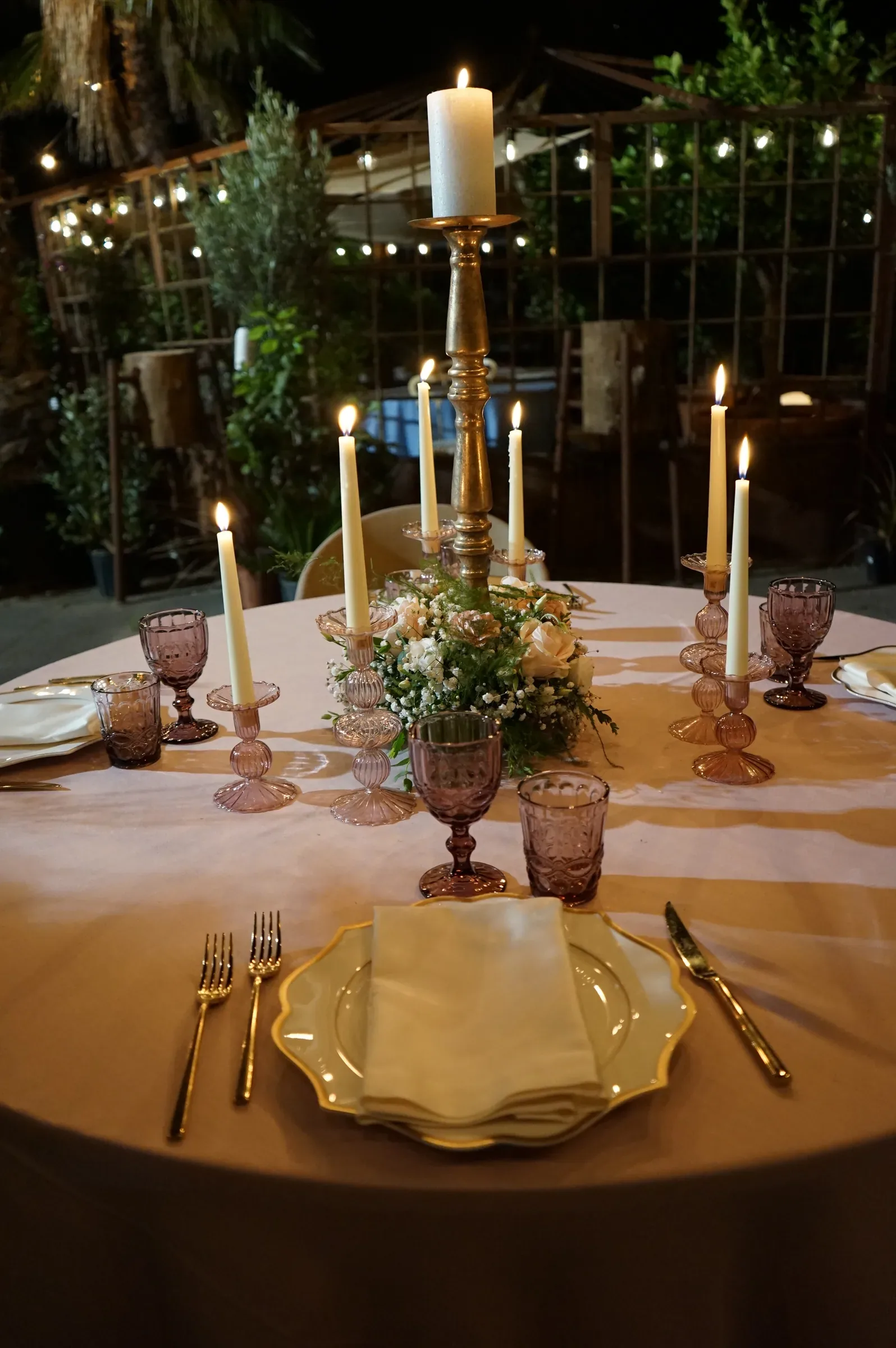 Candelabro dorato e roselline al centro della tavola rosa, di sera