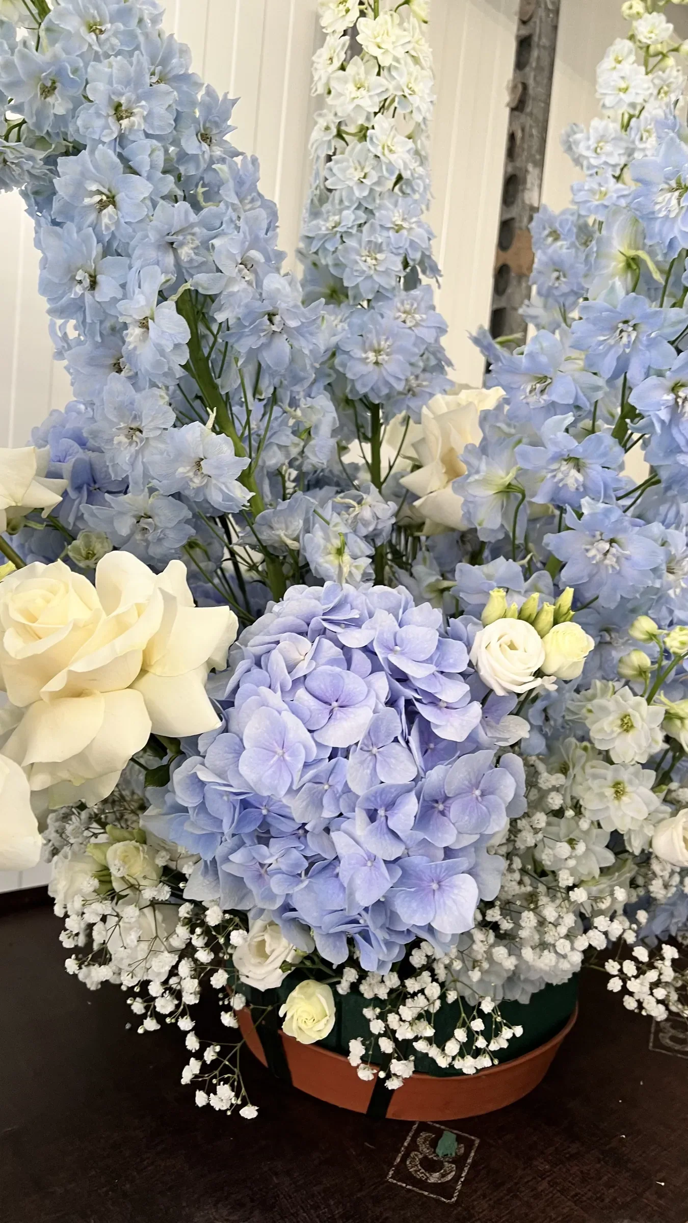Grande composizione con un'ortensia e delphinium azzurri, rose bianche e gypsophila in un vaso basso