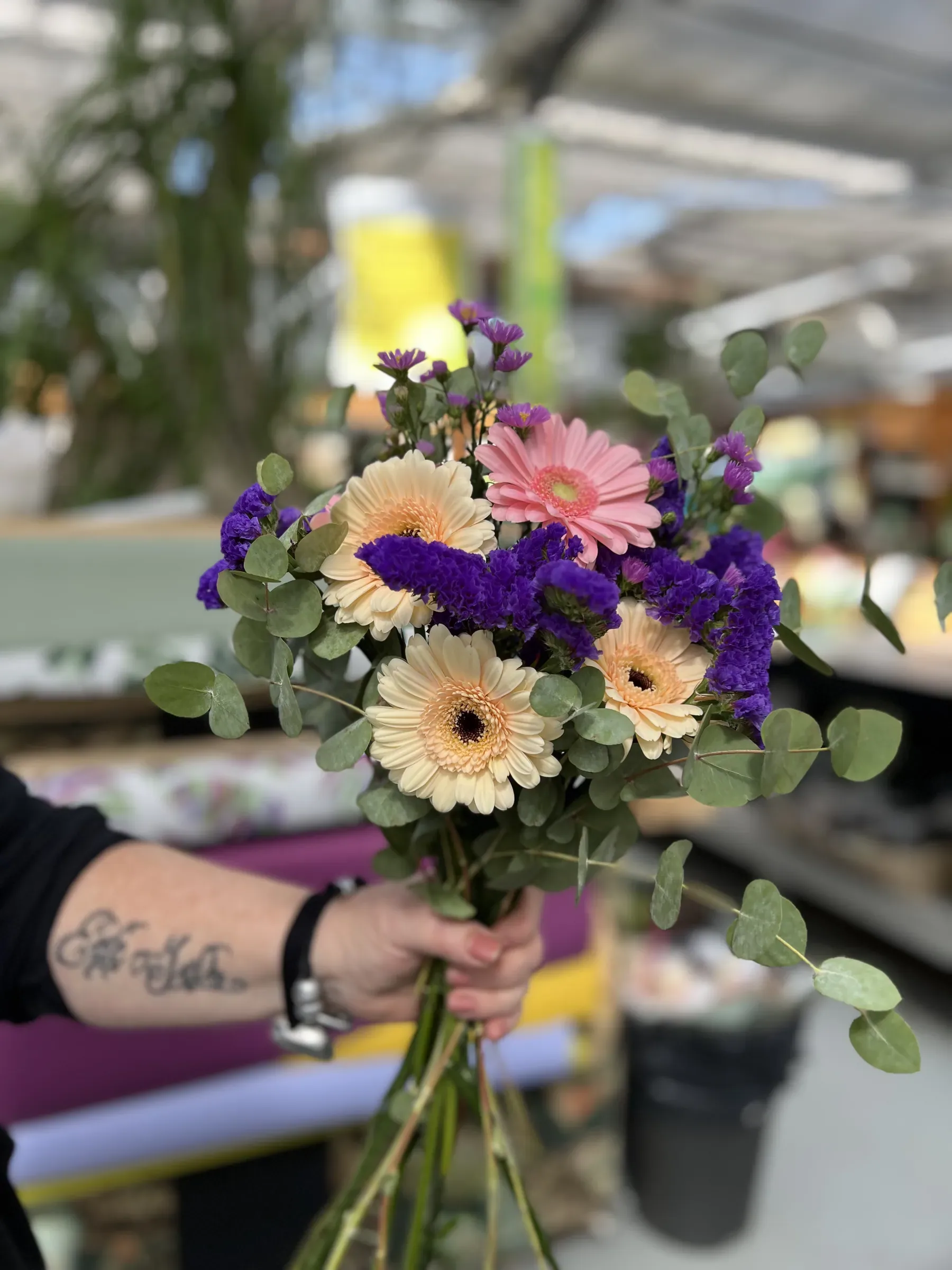 Mazzolino di gerbere color crema e rosa con fiori viola ed eucalipto, tenuto in mano per i gambi