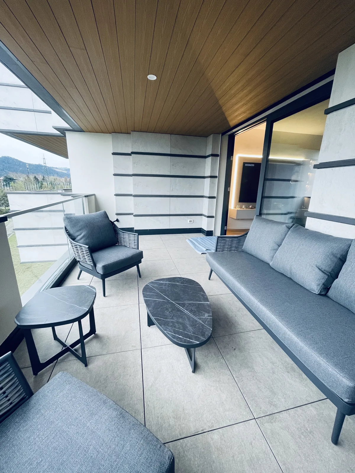 Salotto da esterno grigio su una loggia con il soffitto in legno e il pavimento chiaro