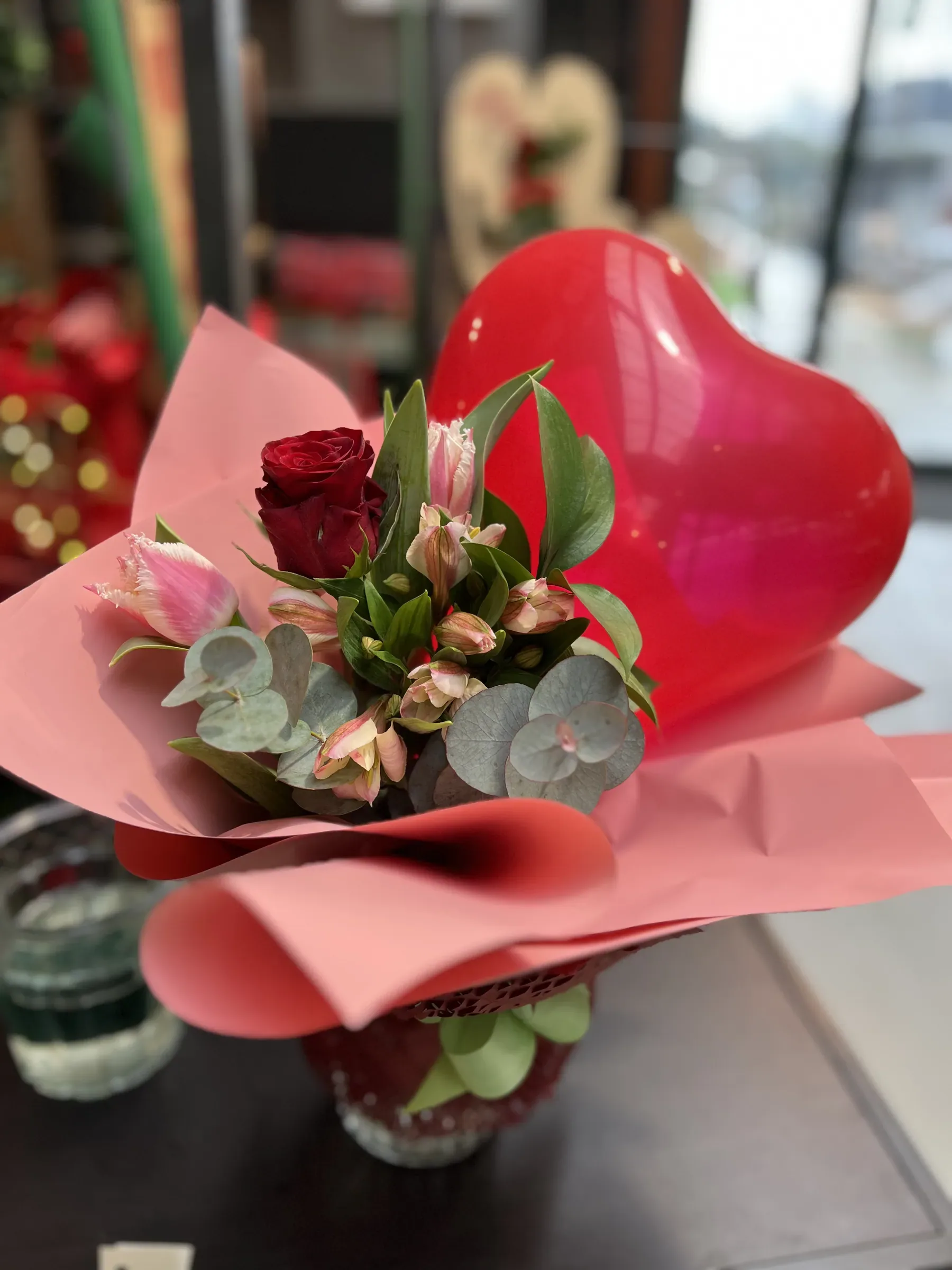 Una rosa rossa, tulipani frangiati rosa, alstroemerie ed eucalipto in un vasetto incartato di rosa, con un palloncino rosso a cuore