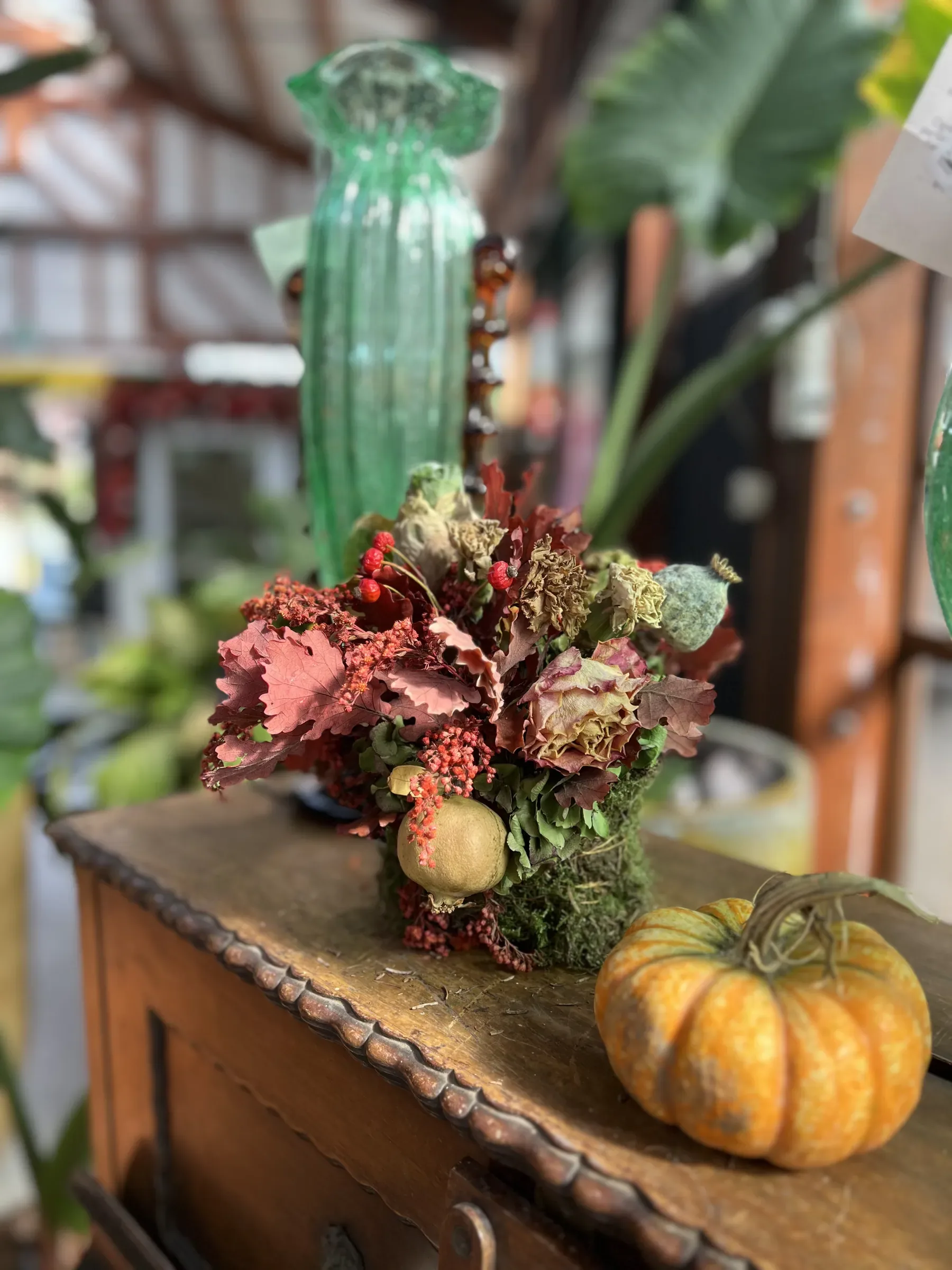Composizione di foglie rosse, bacche e un melograno, con accanto una zucca arancione, su un mobile di legno scolpito