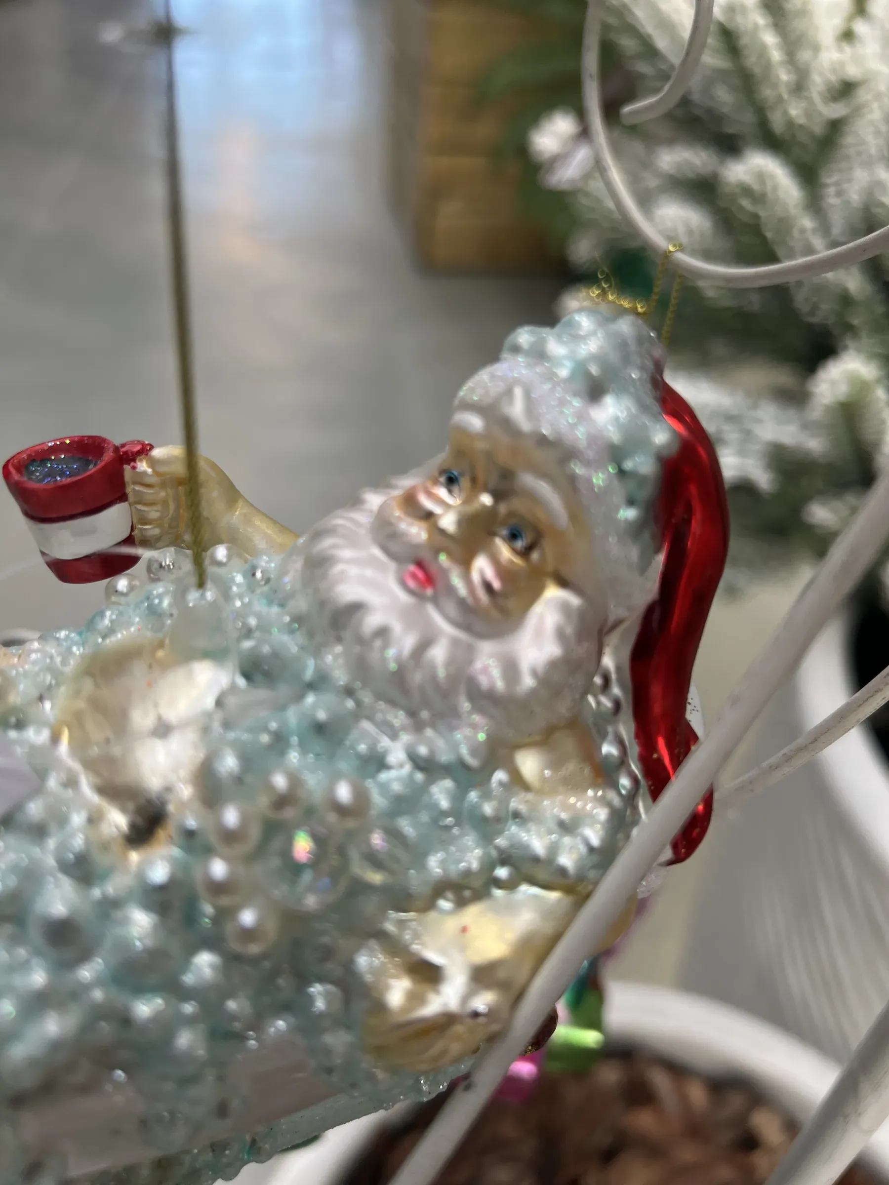 Addobbo di vetro a forma di Babbo Natale nella vasca da bagno piena di bolle, con la tazza in mano, appeso a un espositore bianco