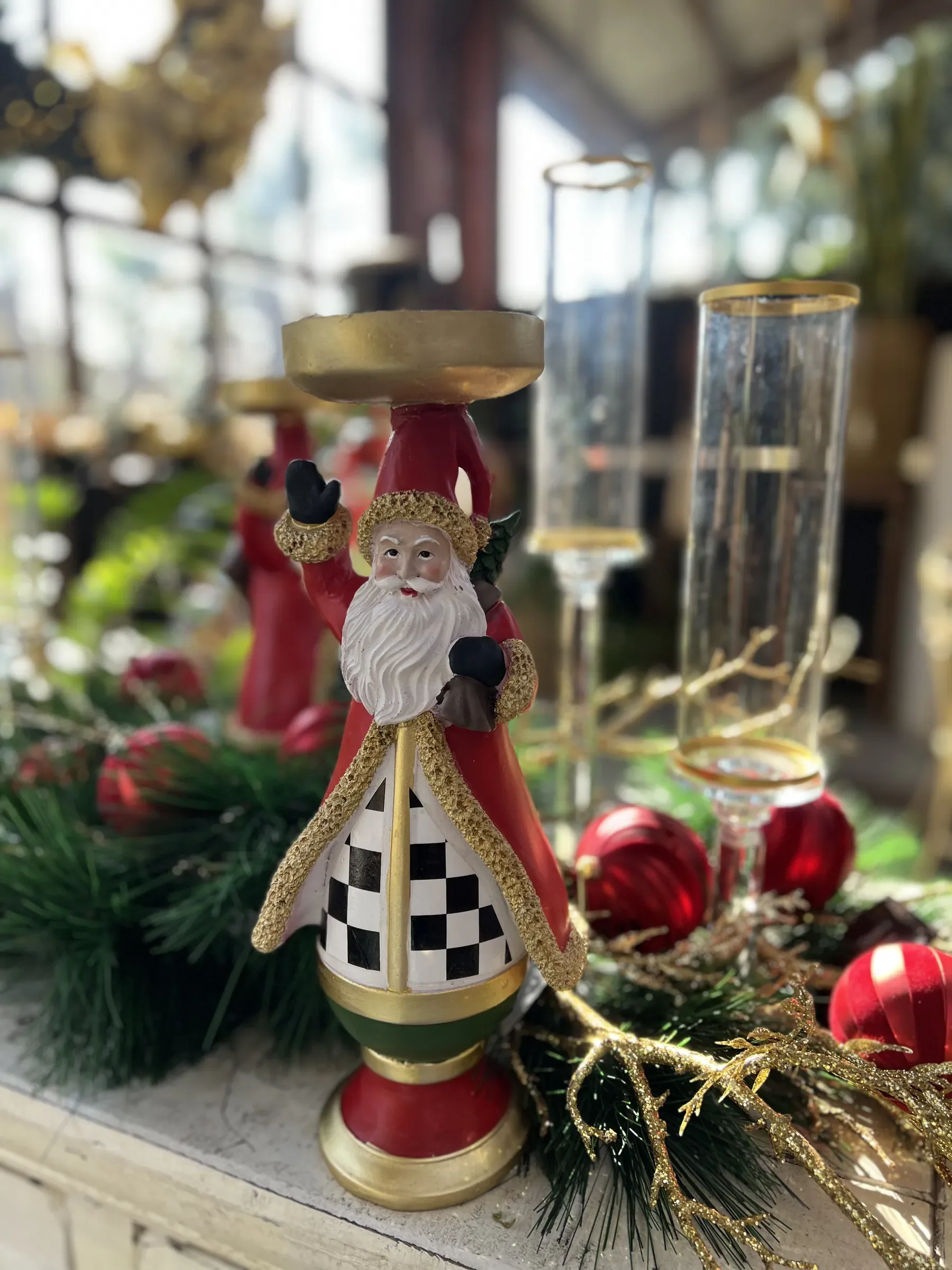 Portacandela a forma di Babbo Natale con la veste a scacchi, fra rami di pino, palline rosse e alti calici di vetro dal bordo dorato