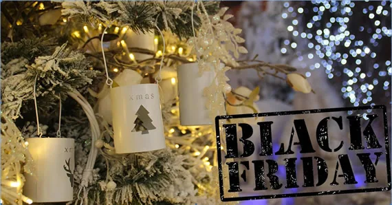 Grafica del Black Friday: lanterne bianche con la scritta xmas e alberelli intagliati appese a un albero di Natale innevato, fra le luci