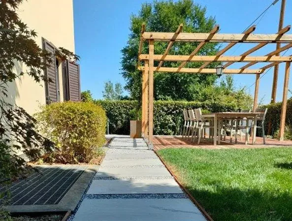 Dopo: pergola in legno sulla nuova pedana a doghe con il tavolo e le sedie, accanto a un camminamento in lastre