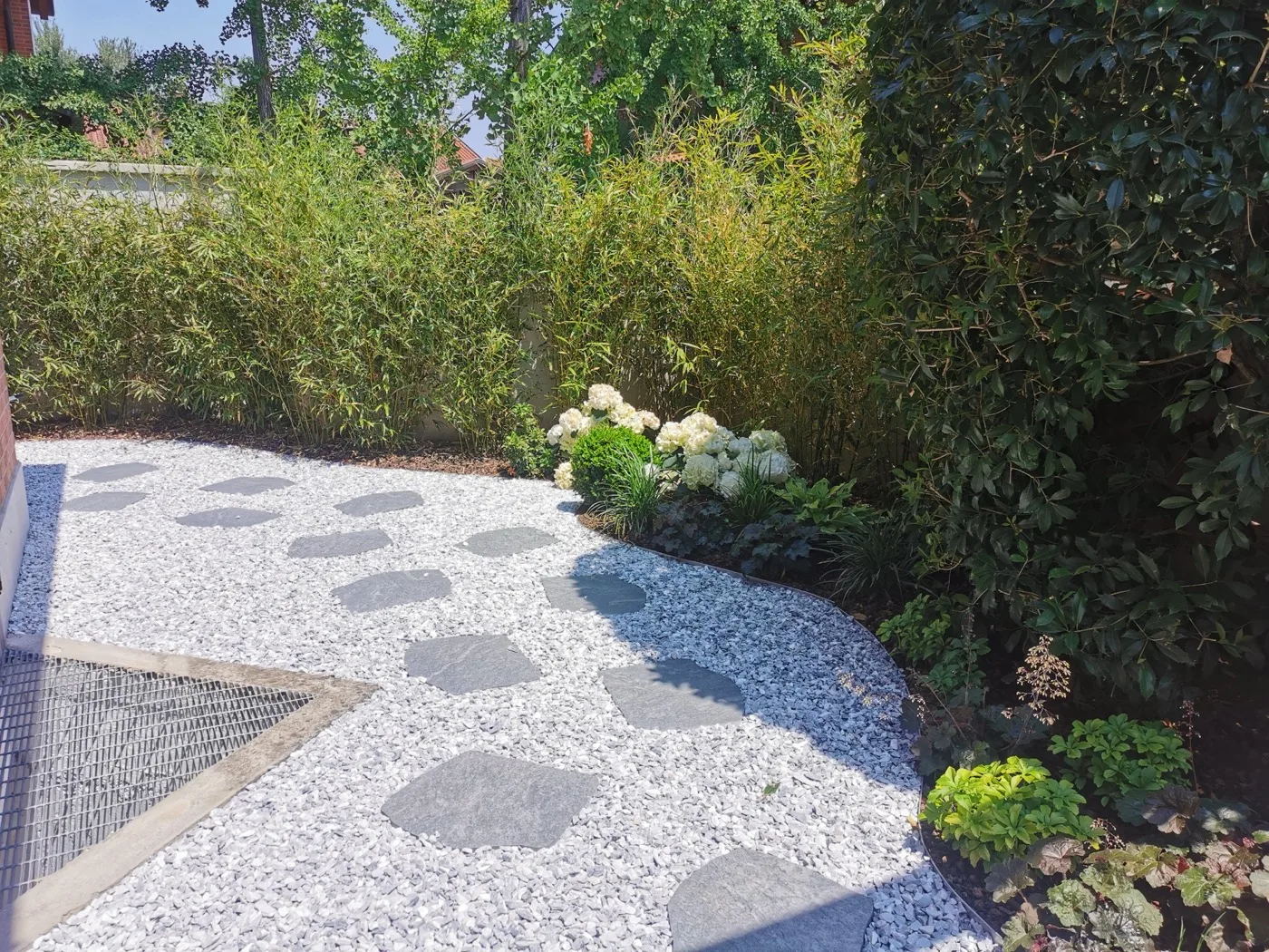 Camminamento di pietre piatte su ghiaia bianca, accanto alle ortensie bianche e a una siepe di bambù