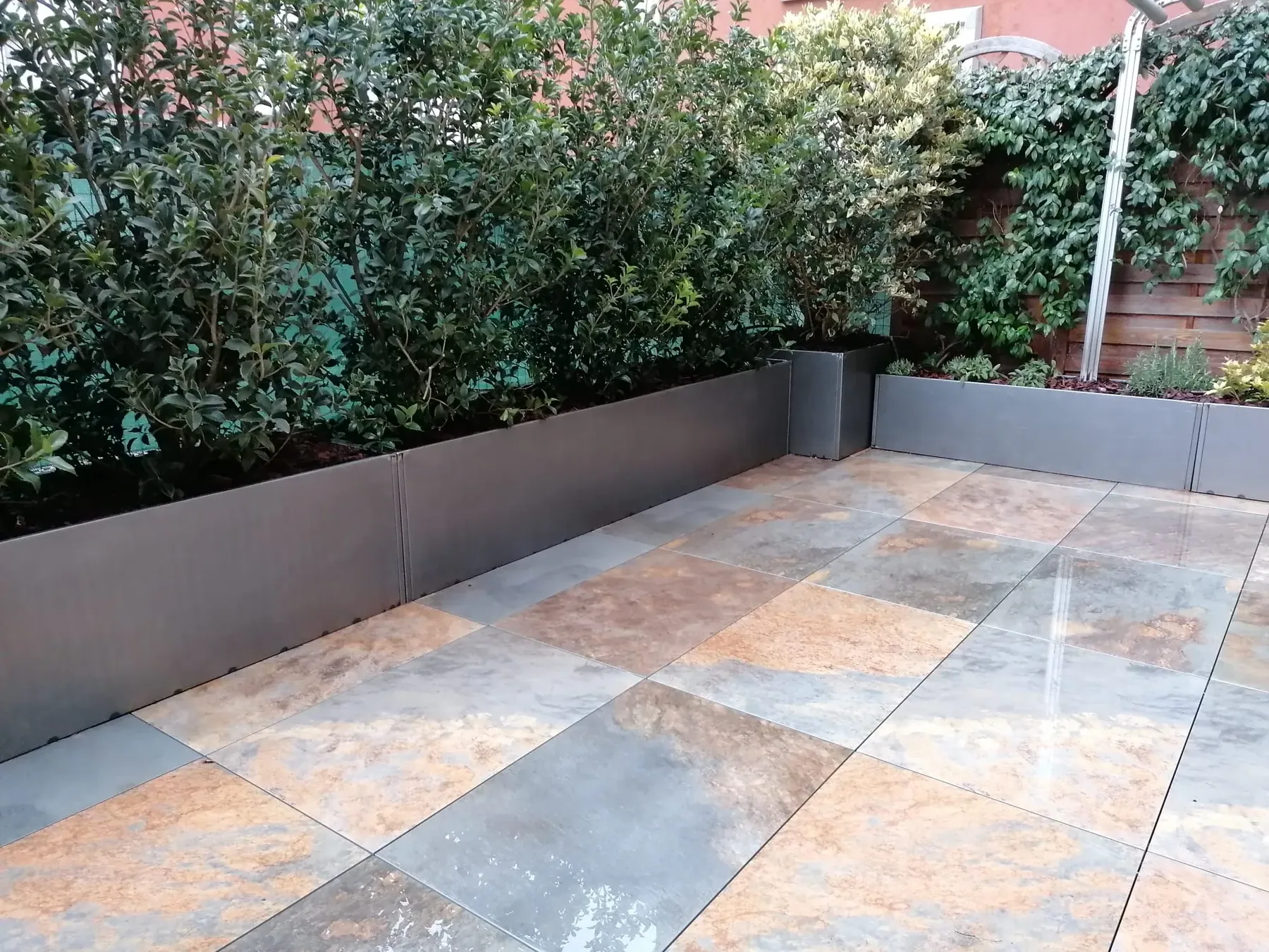 Terrazzo pavimentato in grandi lastre dai toni dell'ardesia, con fioriere grigie di arbusti sempreverdi lungo il parapetto