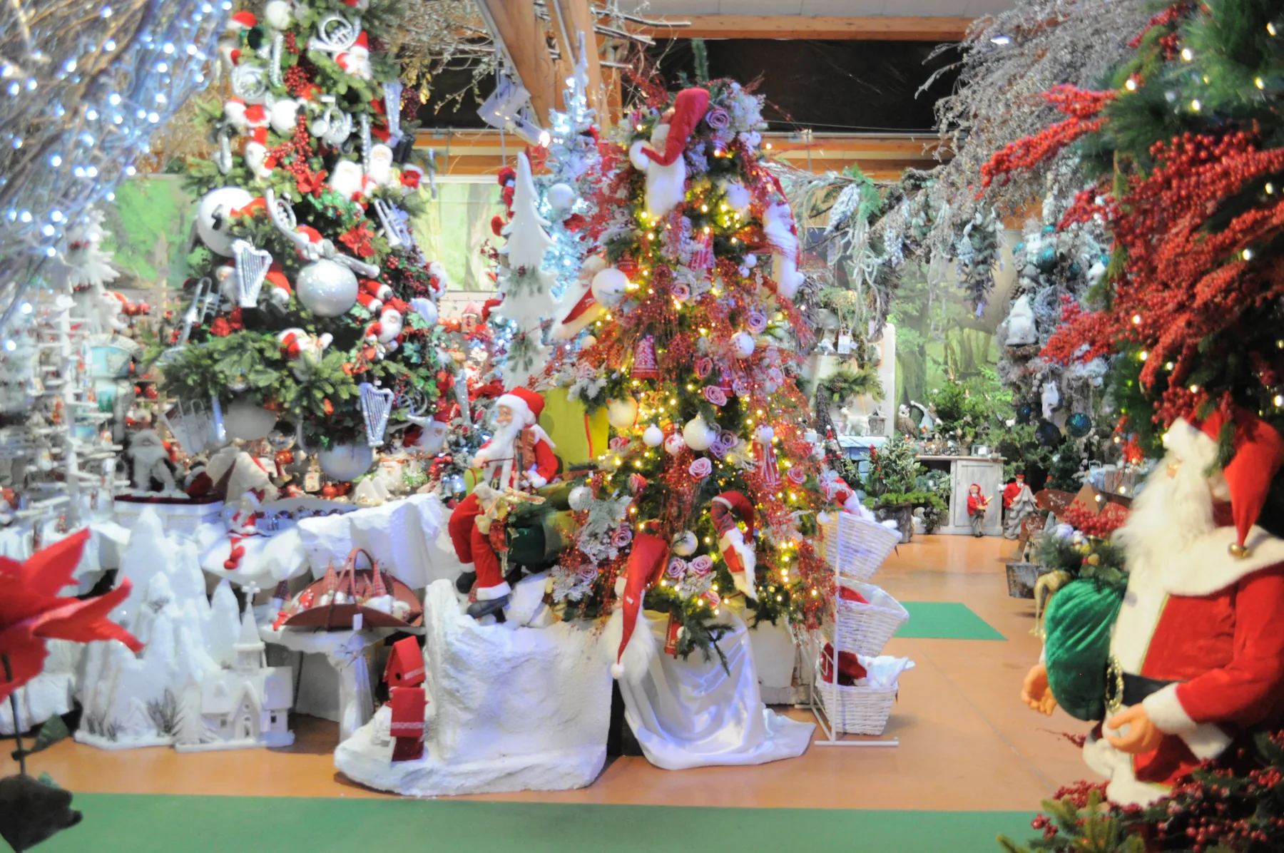 Albero addobbato di rosso e bianco fra teli bianchi a finta neve, con pupazzi di Babbo Natale e altri alberi decorati