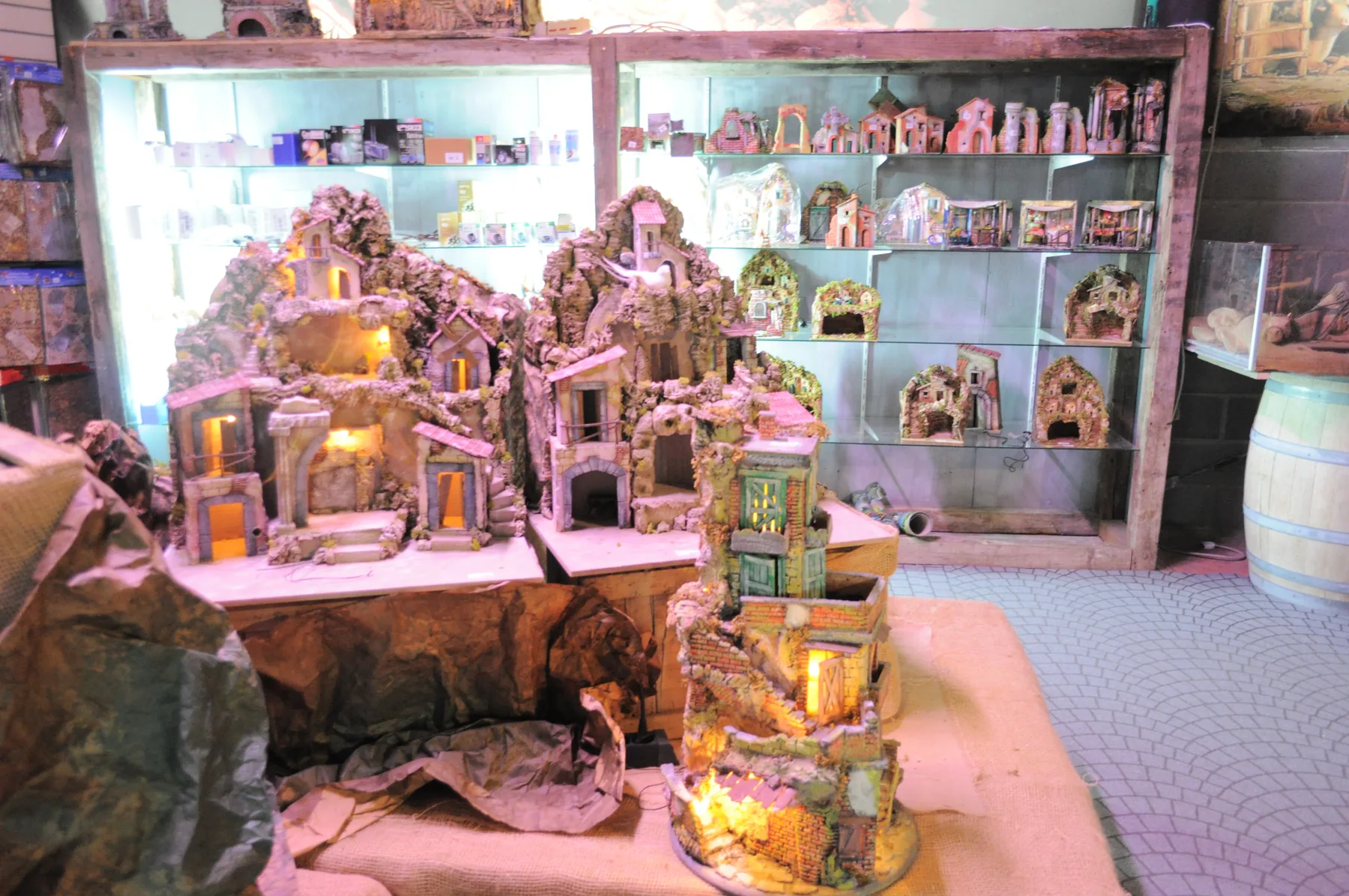 Casette e borghi da presepe illuminati su un banco, davanti agli scaffali di altri pezzi