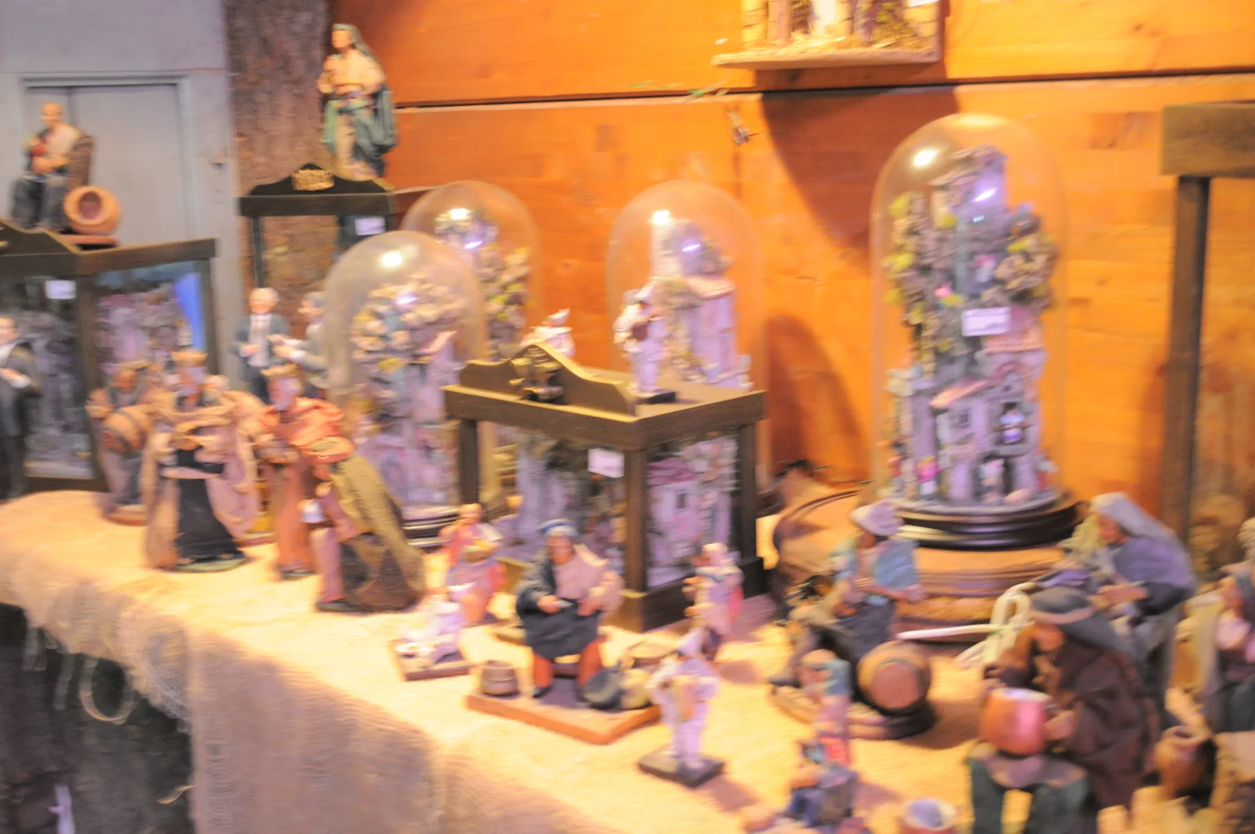 Statuine da presepe di pastori e contadini su un tavolo, fra campane di vetro con borghi in miniatura