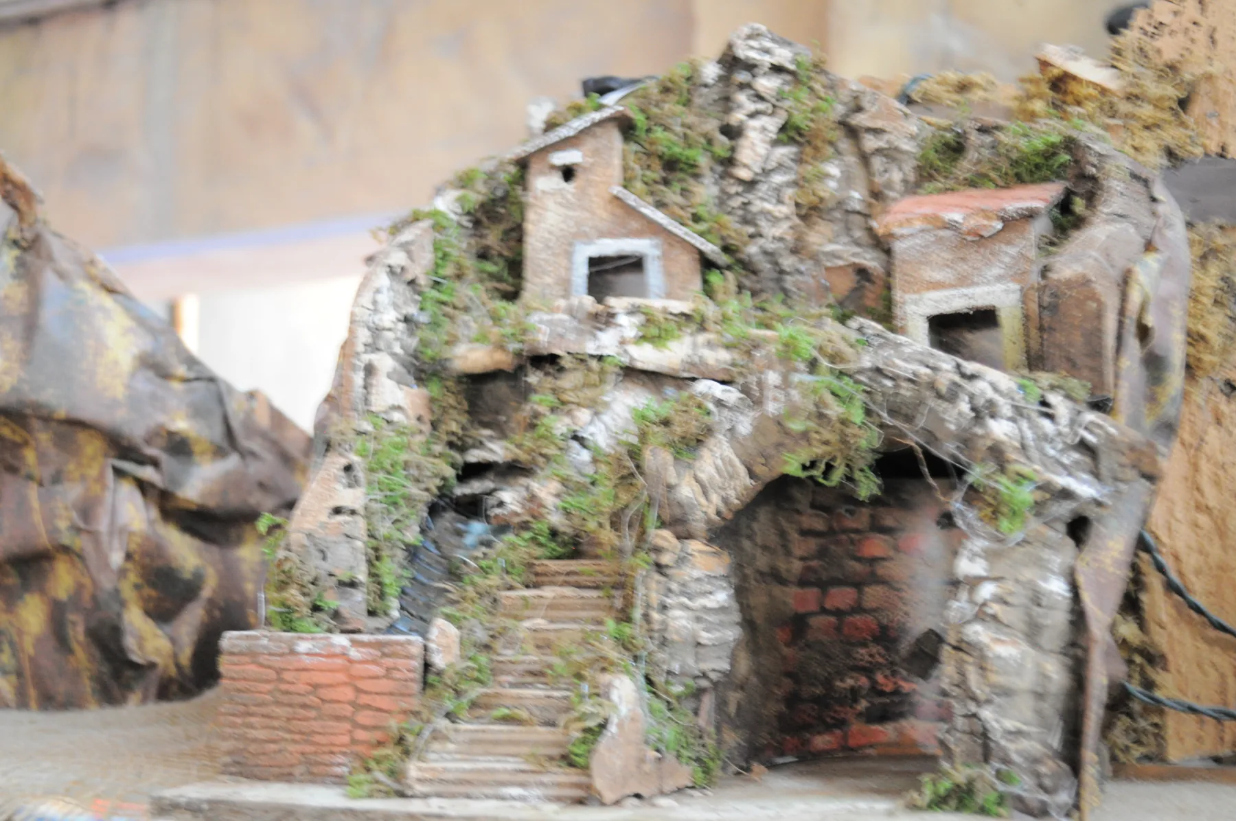 Grotta da presepe in finta roccia con muschio, una scalinata, un arco di mattoni e due casette in cima