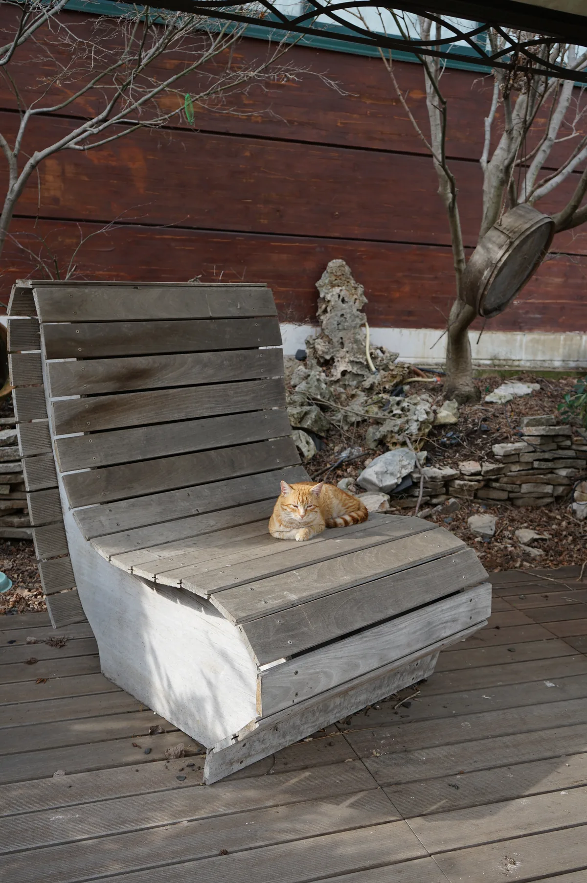 Sdraio in doghe di legno grigio su una pedana di legno, con un gatto rosso addormentato sopra