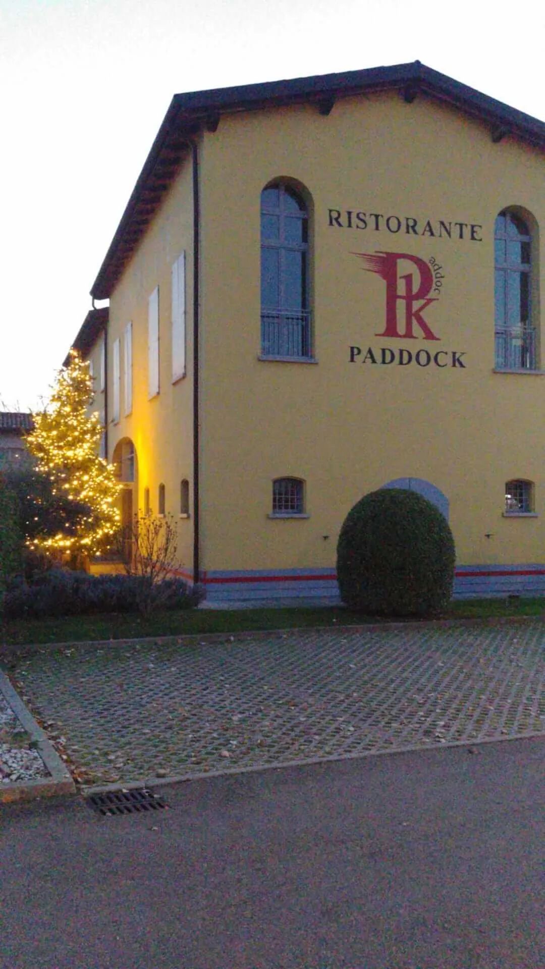 Edificio giallo del Ristorante Paddock al tramonto, con un albero di luci accese accanto all'ingresso