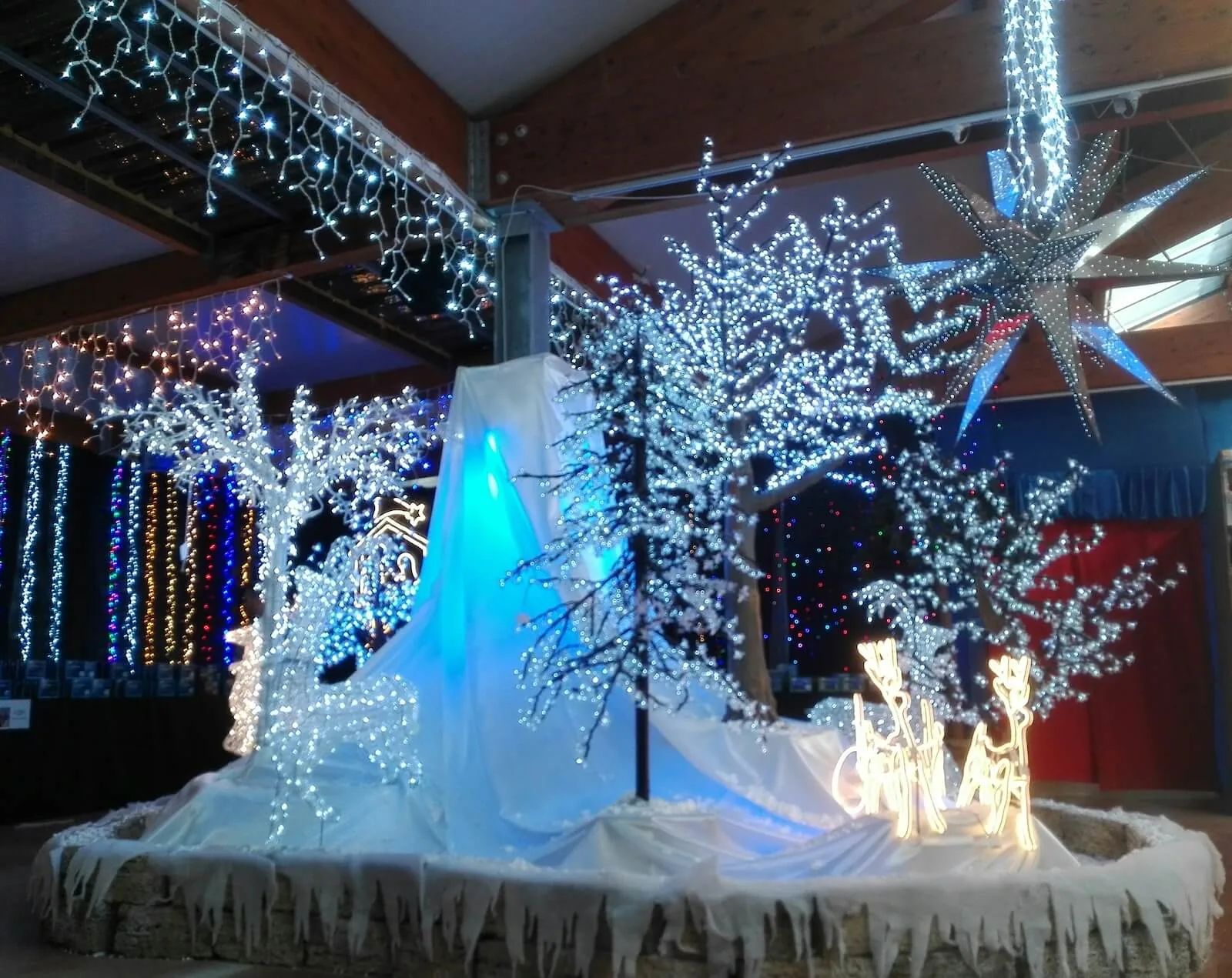 Basamento tondo in pietra coperto da un telo bianco, con alberi di luci, renne luminose e una grande stella appesa