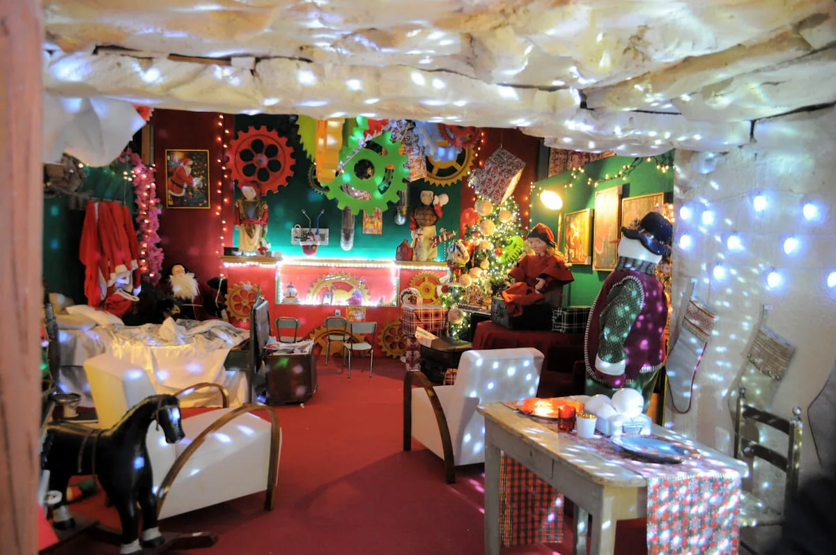 Salotto di Babbo Natale con poltrone bianche, ingranaggi colorati alle pareti e luci sul soffitto innevato