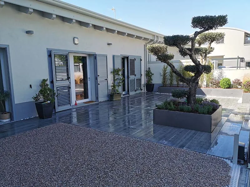 Terrazzo pavimentato con un grande riquadro di ghiaia e una fioriera grigia con un albero potato a nuvole