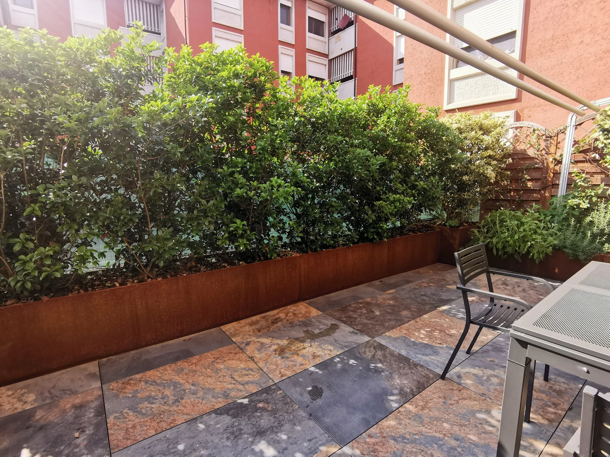 Fioriere in corten con la siepe sempreverde e la pavimentazione in lastre di pietra, con il tavolo sul lato