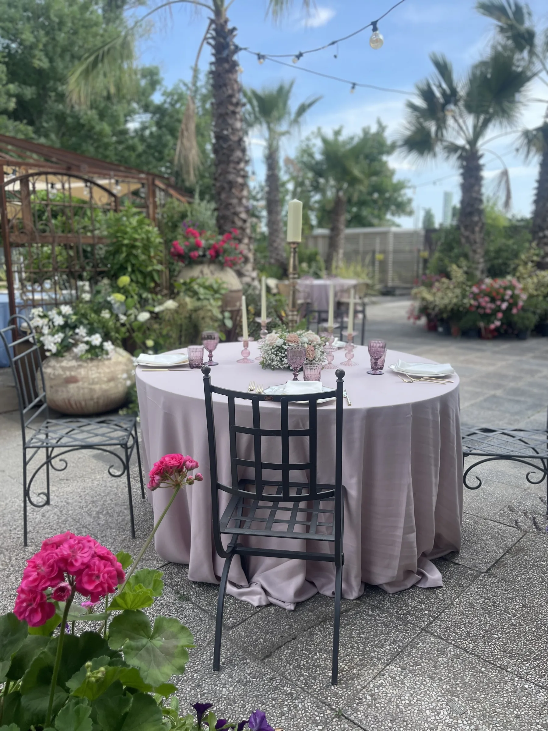 Tavola con la tovaglia rosa antico e una sedia di metallo scuro, con gerani fucsia in primo piano